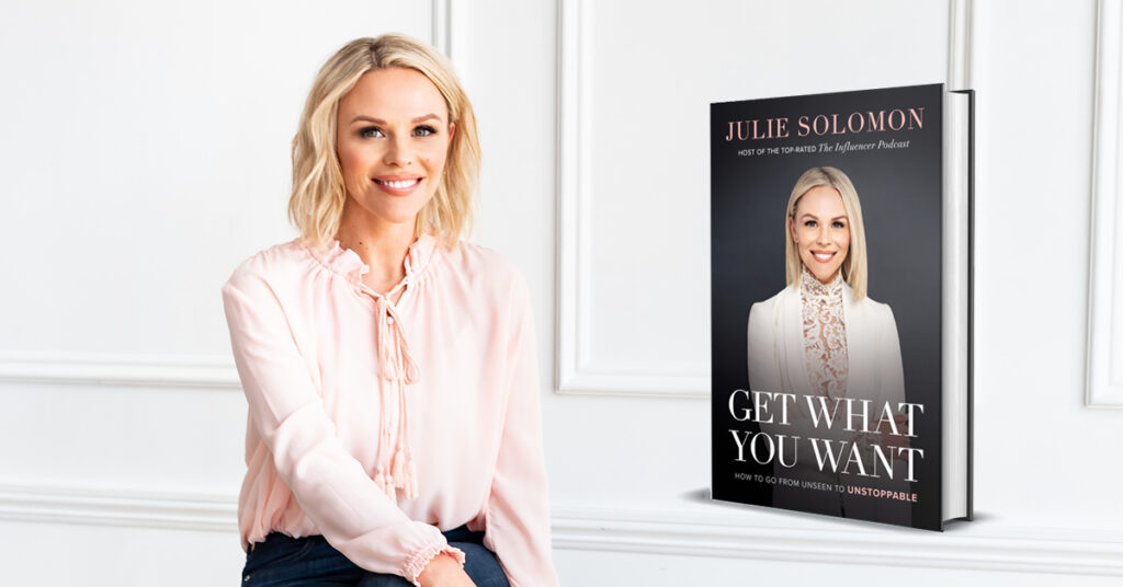 Julie Solomon sitting in a white room, with the cover of "Get What You Want"